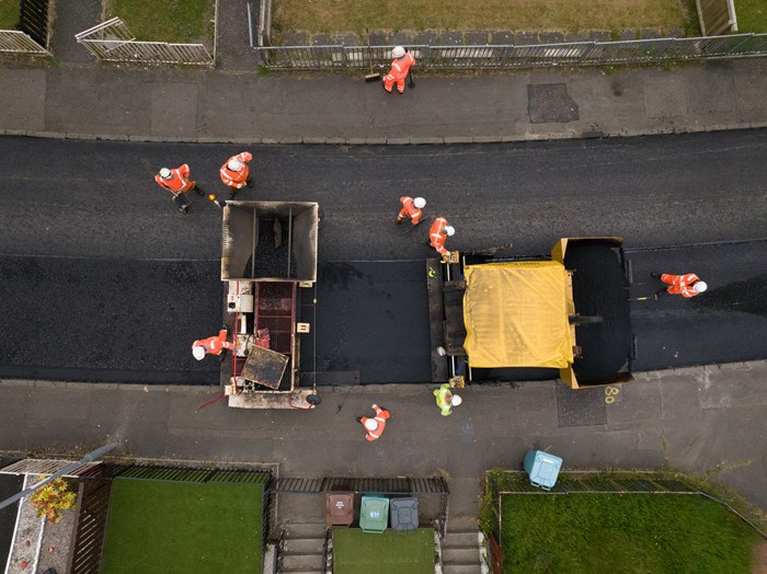 Aerial photograph of a road maintenance team in high-visibility orange overalls resurfacing a road