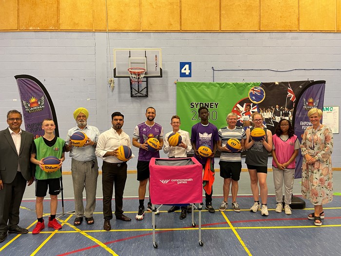 A group of people smiling at the camera and holding basketballs in a sports hall