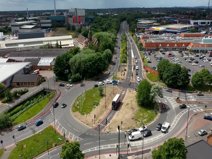 Aerial view looking down on a roundabout on a clear day. The roundabout has a road cutting through the middle linking two dual carriageways and a bus is driving through this. Other traffic circles around the outside of the roundabout.