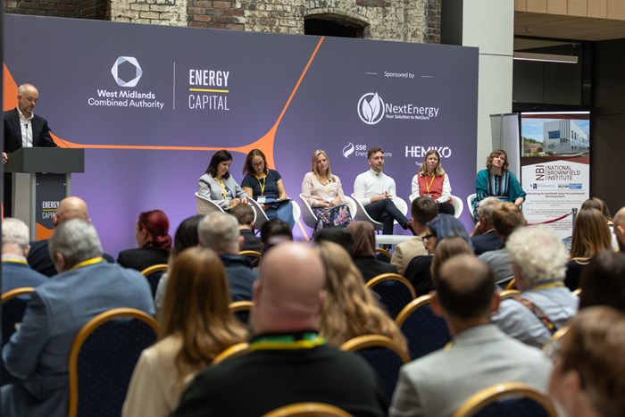 A panel of 6 people on the stage at the conference
