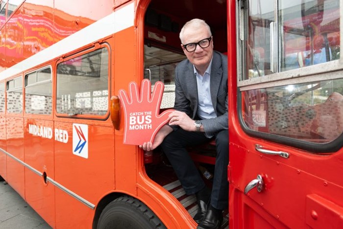 Mayor Richard Parker leaning out of the doorway of a red bus waving a 'Catch the Bus' foam hand