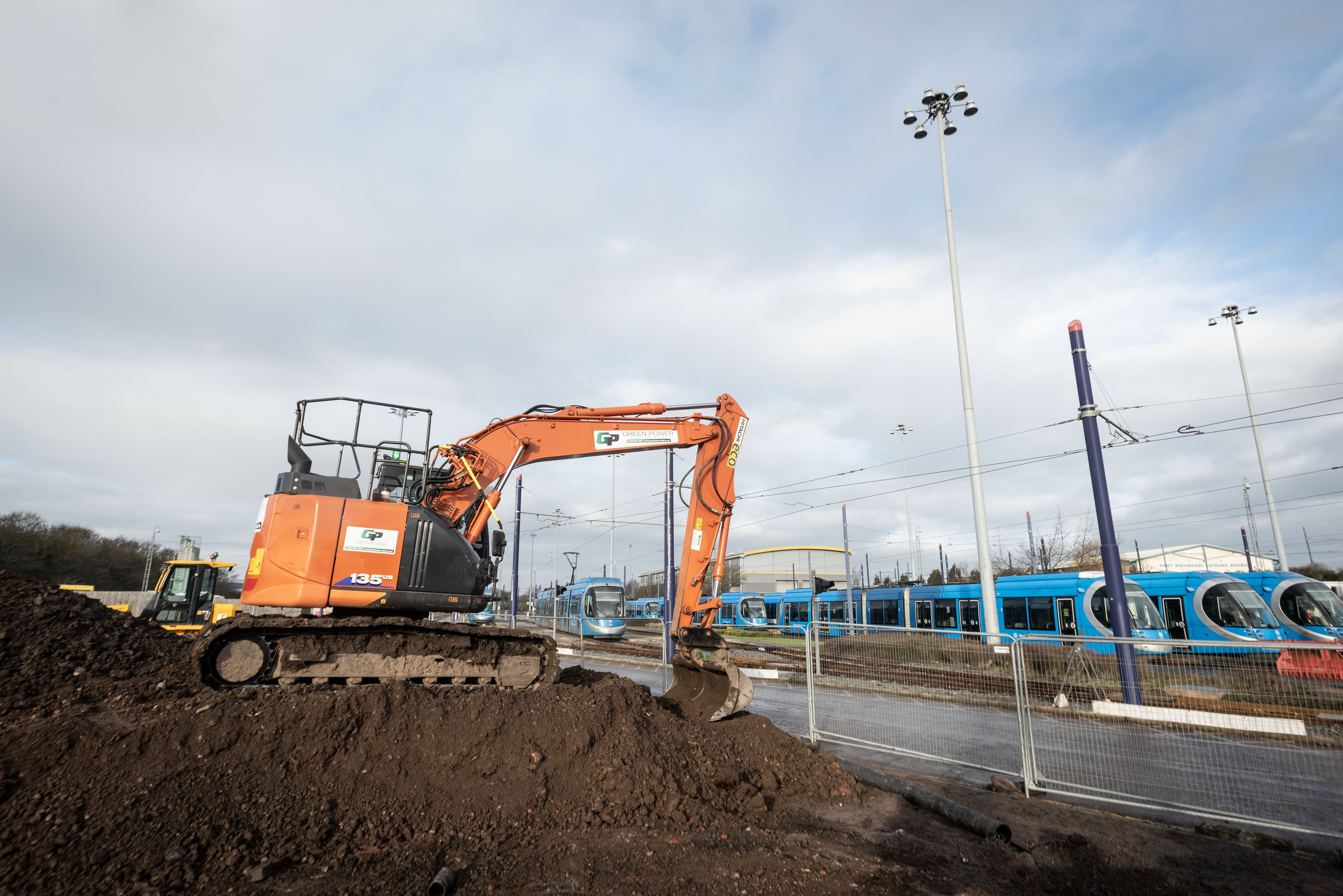 Digger working on land next to parked blue Metro trams at the depot
