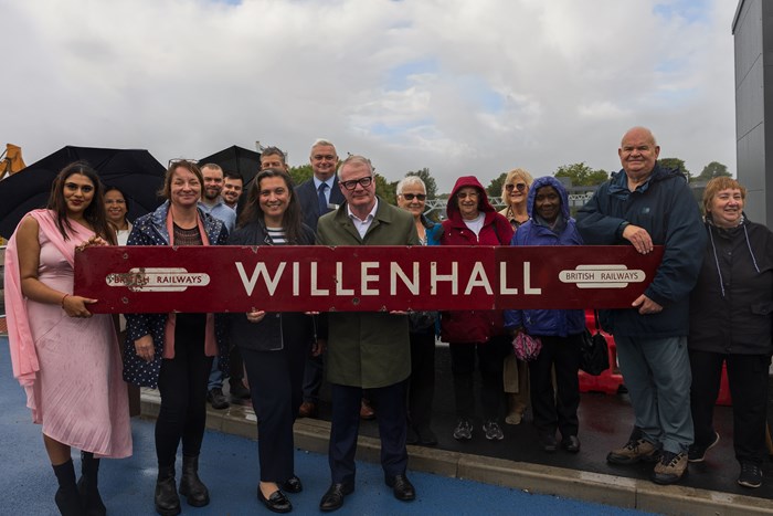 A group of about a dozen people - members of the Willenhall community - are gathered on a grey cloudy day. At the front of the group a large nine foot long sign saying "Willenhall" and British Railways is being held. The sign is a deep red with white writing. In the centre of the group is Mayor of the West Midlands Richard Parker.