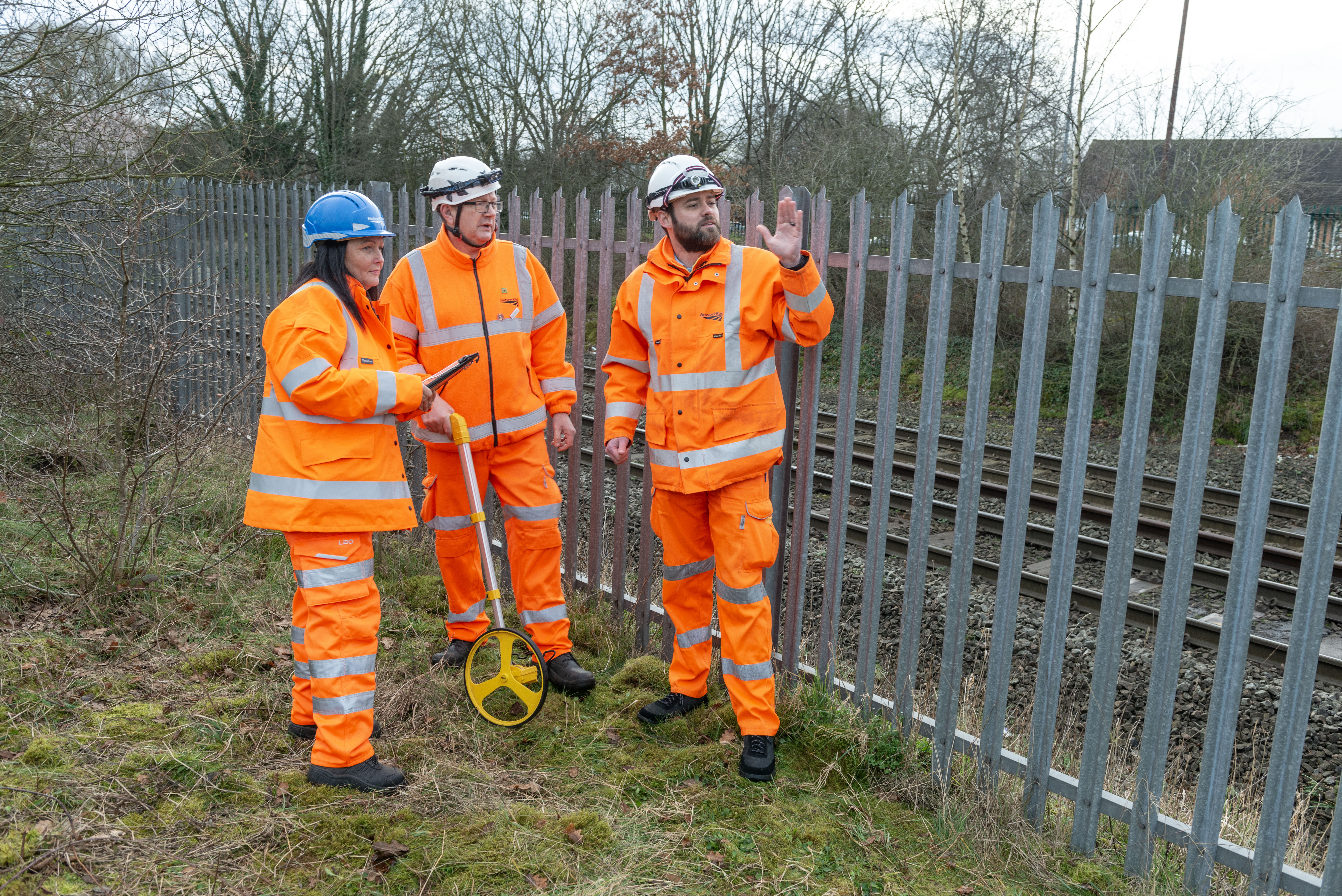 Group of three rail engineers in hi-vis outfits and hard hats carrying out survey and assessment work on the site