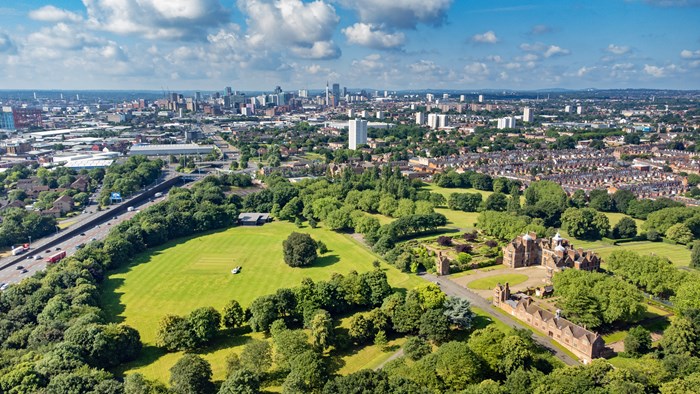 Aerial view of Birmingham with a large green park, historic red-brick building, and city skyline under a blue sky
