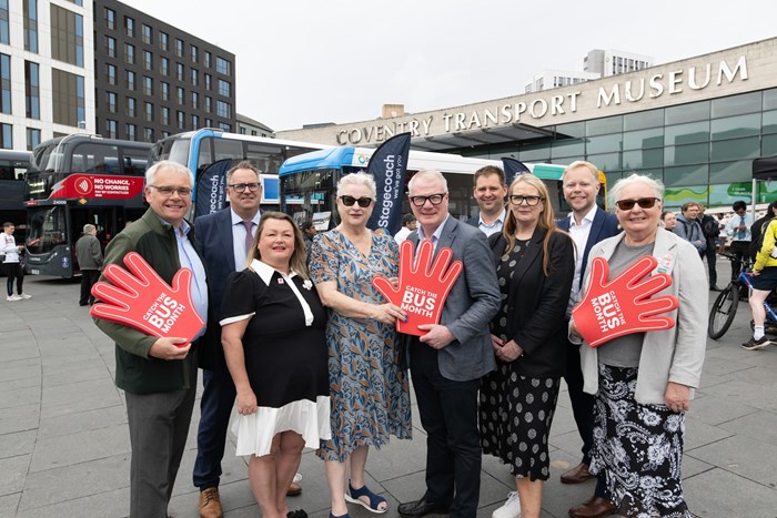 Group of people waving red foam hands in front of buses outside the Coventry Transport Museum