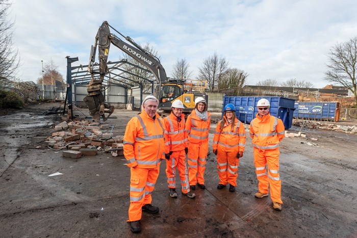 Rail bosses overlooking site with digger and frame of industrial unit being demolished