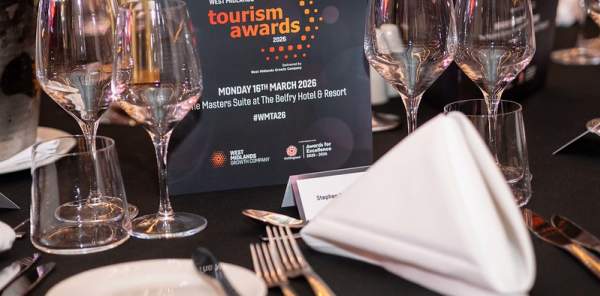 Formal dining setup with wine glasses and napkins on a black table. A tourism awards event card is prominently displayed, creating an elegant ambiance.