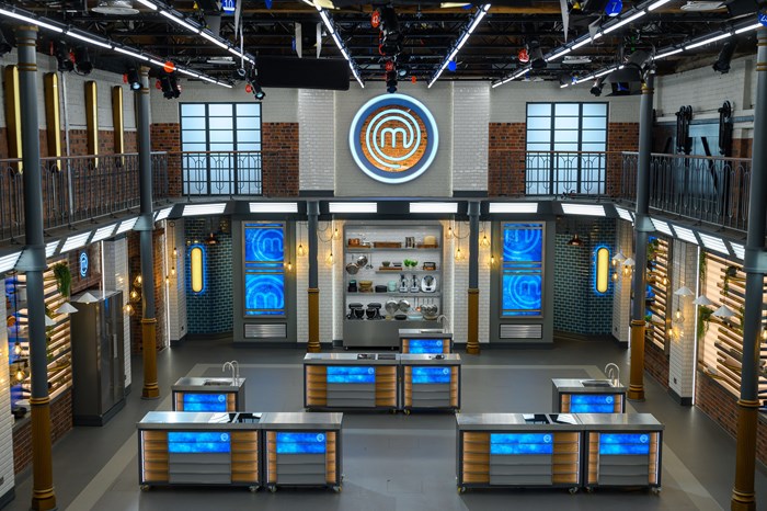 A photograph of the new MasterChef studios with the MasterChef logo on the facing wall in the centre behind cooking stations that will be used by contestants on the TV show.