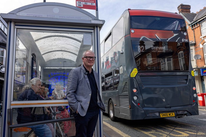 Mayor Richard Parker waits next to a bus shelter. A number 82 bus is pulling away