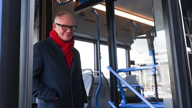 Photo is of the doorway of a blue trimmed bus - it shows Mayor Richard Parker in a black overcoat and red scarft standing on the steps about to get on.