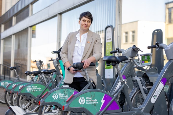 Photograph of a female stood next to a bike. There are bikes in front and behind her.