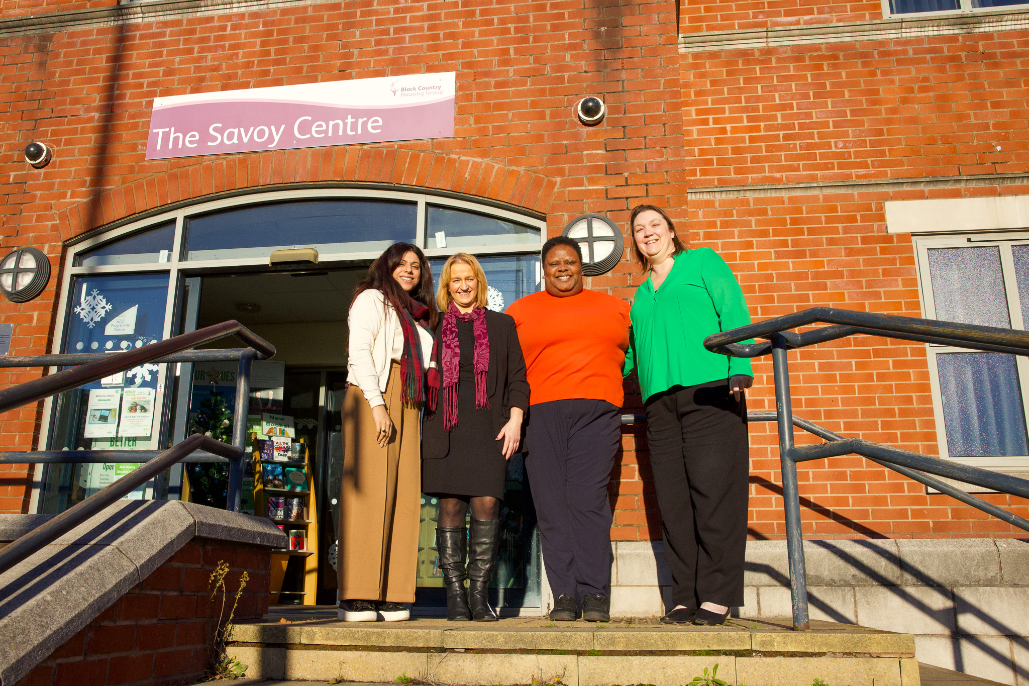 Four people stand smiling on the steps of The Savoy Centre, against a brick wall backdrop.