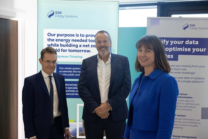 Three people smiling at the camera with company banners in the background