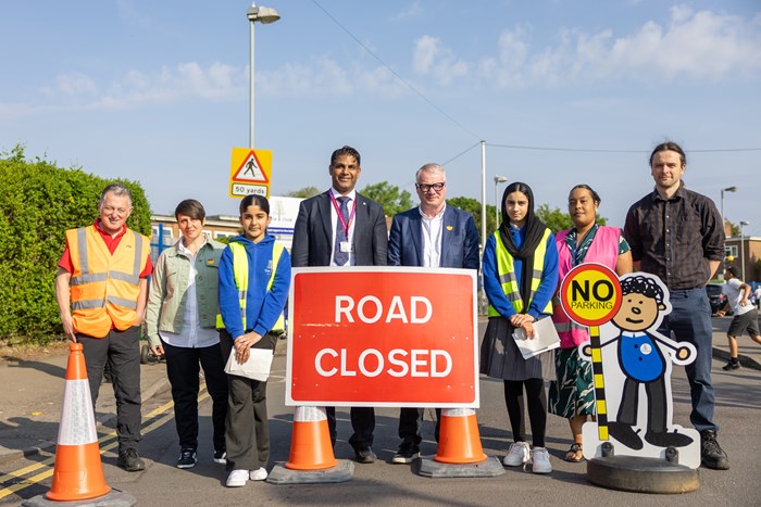 Group of people, including school children standing behind a road closed sign