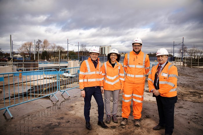 the four VIPs in orange hi-vis and hard hat outfits on the delta junction structure with the existing tram line in the background