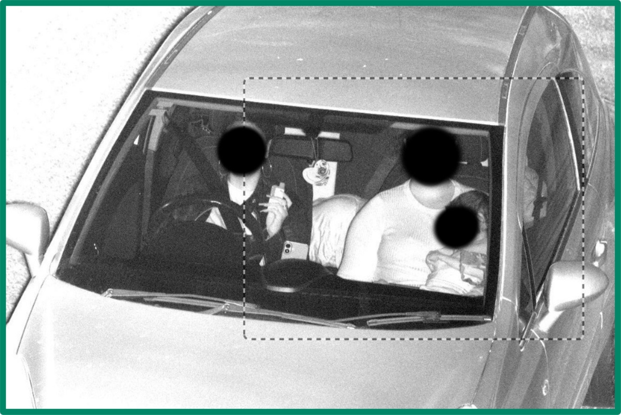 Black and white security camera image shot through car front window shows passenger with small child on lap and no seatbelt on