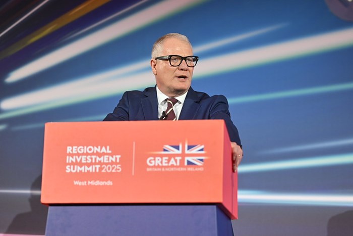 A speaker at the Regional Investment Summit 2025 in West Midlands stands at a podium decorated with a British flag backdrop.