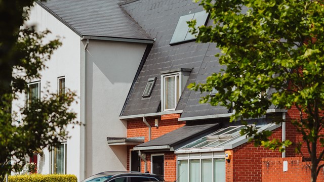 An image of a newly built home with cars in the driveway. The building can be seen throught the leaves of green trees.