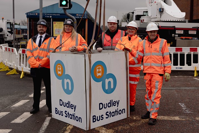 Five people in bright orange hi-vis construction outfits with the old Bus Station sign taken from a pole high above the bus station