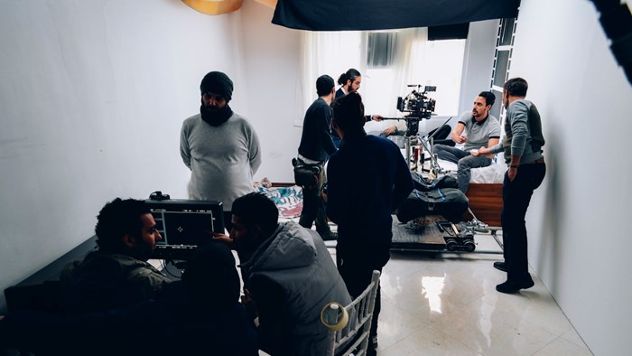A film crew position cameras as they prepare to film a piece to camera with a person lying on a bed