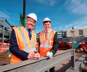 Two people in a hi visibility vests and helmets outside a construction site.
