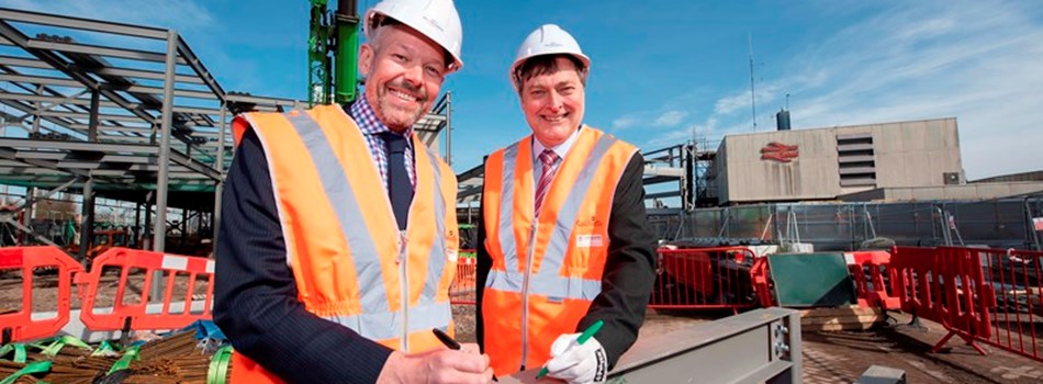 Two people in a hi visibility vests and helmets outside a construction site.