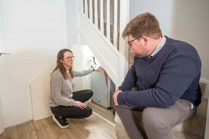 A woman discussing an electrical unit with a man. She holds the unit which is installed in a cupboard beneath the staircase.