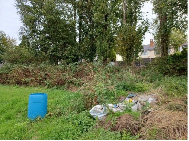 The image shows an overgrown field with grass and bushes to the right and flytipped waste in the middle