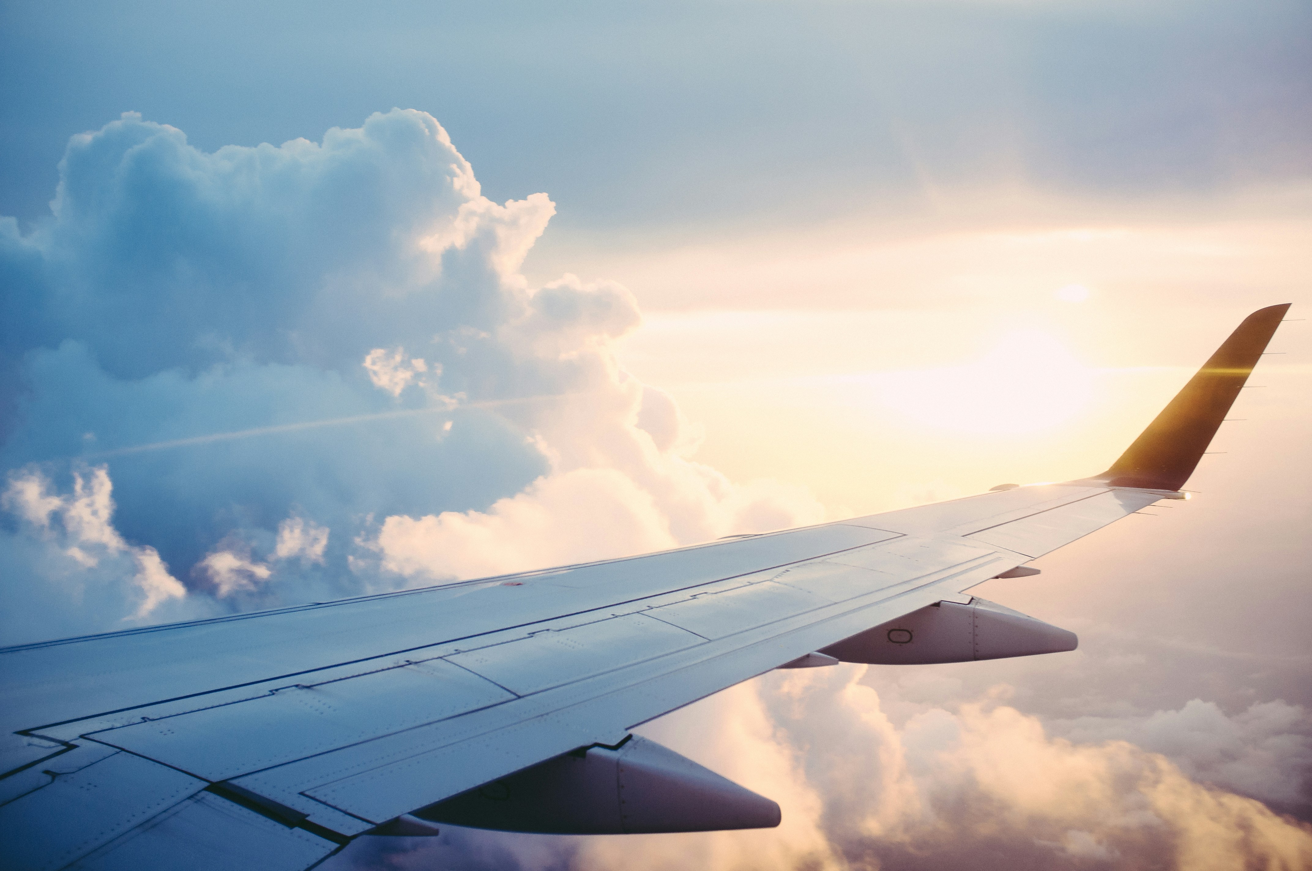 The wing of a plane in the sky with clouds and the sun setting in the background