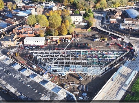 Aerial shot overlooking a large town centre construction site. A trapezium shaped steel frame dominates the image. And tram line runs along the side with a stop next to the frame building.