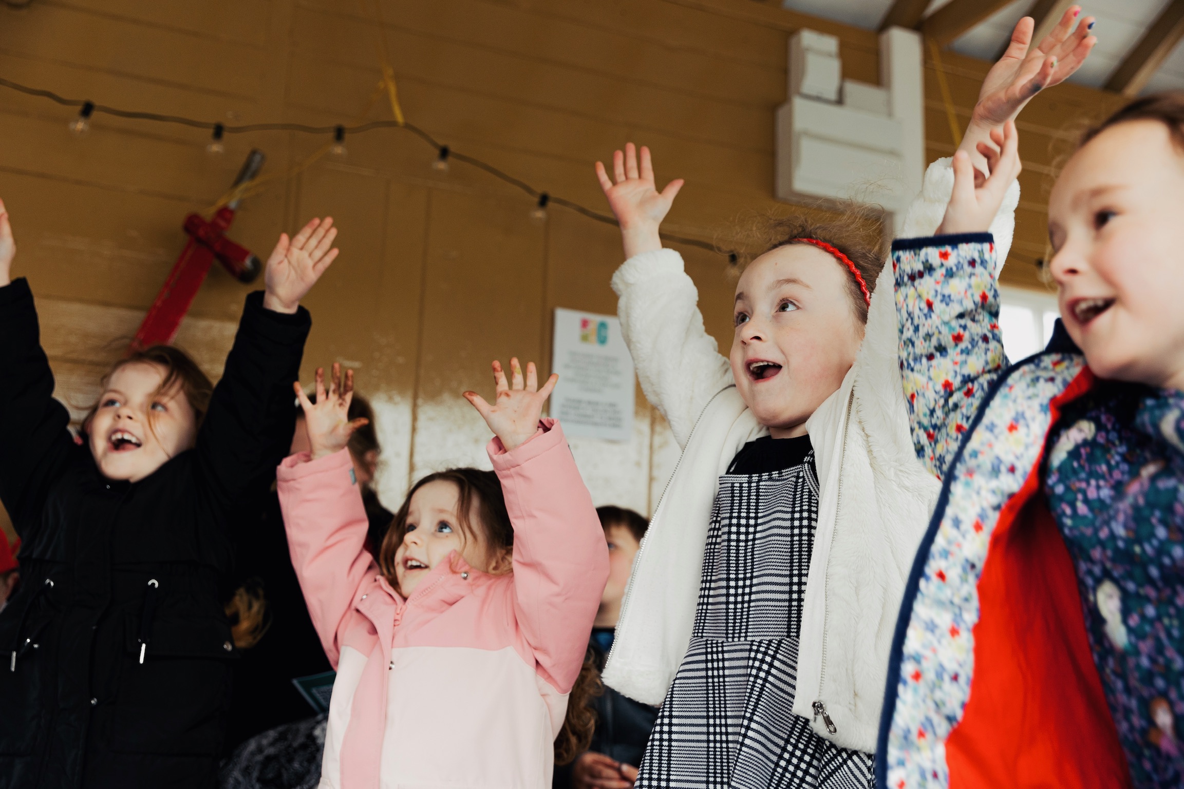 An photograph of four young children having fun with their arms outstretched in the air.