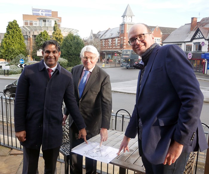 Three politicians pointing at plans laid out on table with Sutton Coldfield town centre Parade roundabout in the background