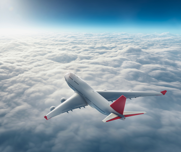 A white airplane with red wing tips flying above the clouds.
