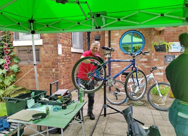 A person fixing a bike stood under a green gazebo