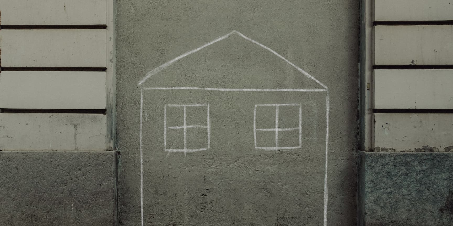 Simple chalk drawing of a house with two windows on a gray wall between sections of white and gray paneling