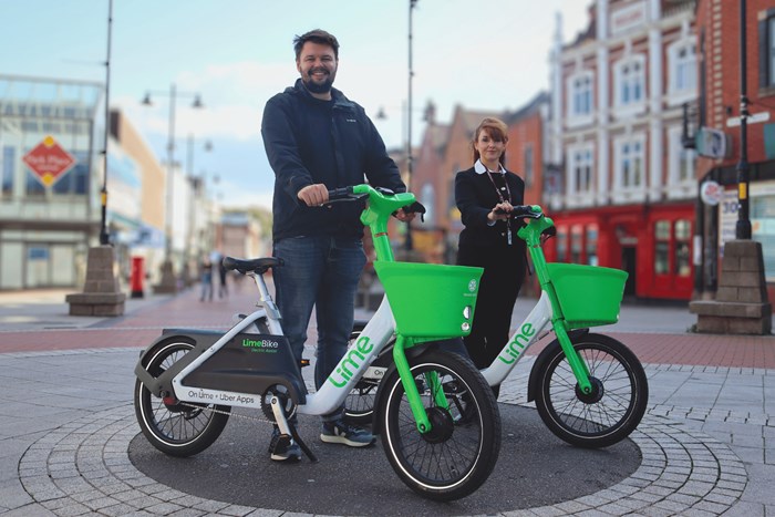 Two people standing alongside green and white bicycles in a town centre high street