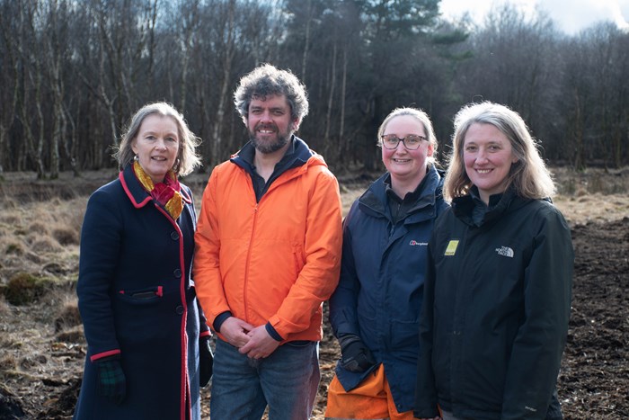 Four people standing in a line in a field with trees in the background