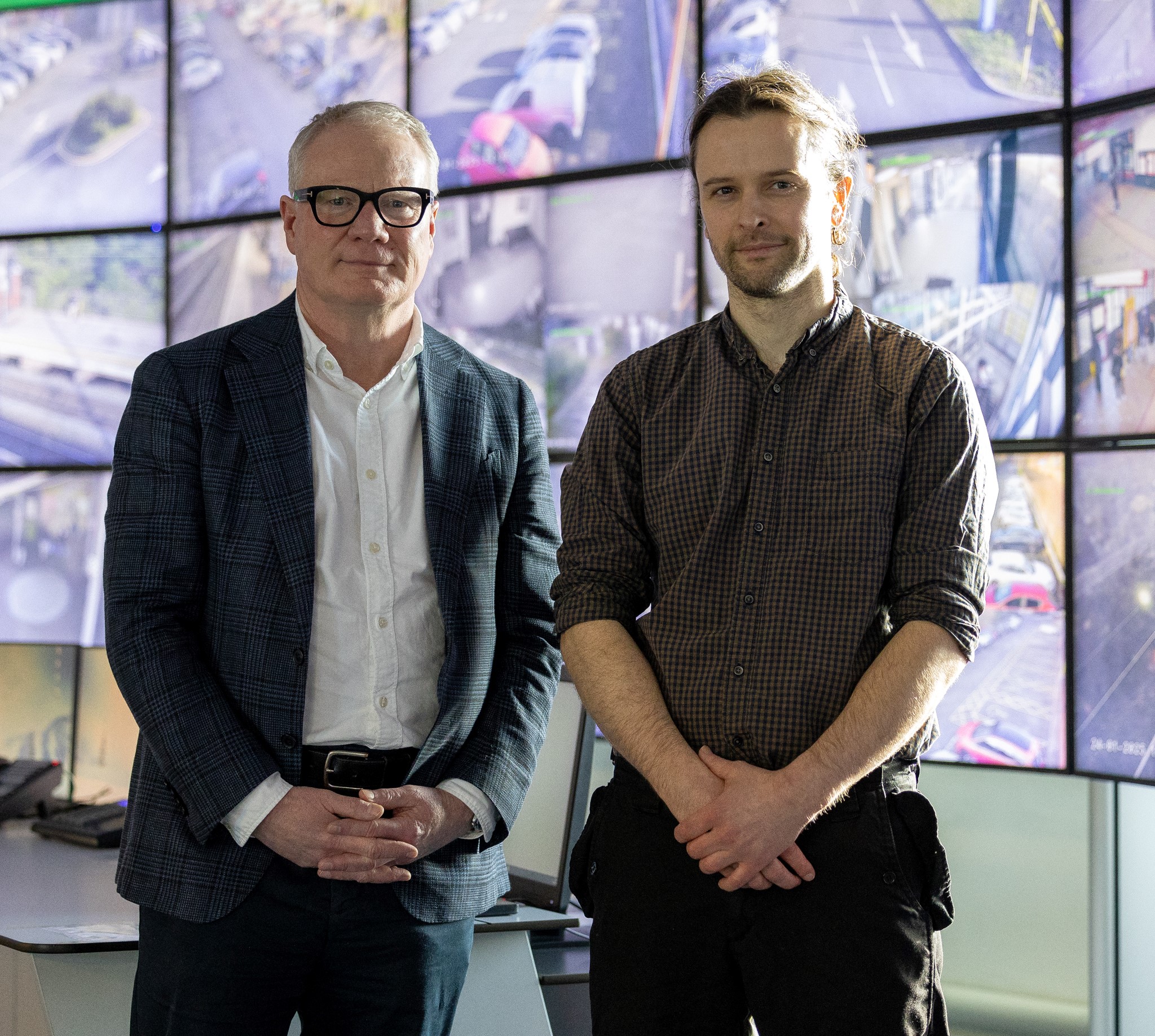 Two men standing in front of wall of screens showing cctv camera images