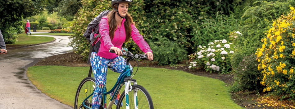 A woman wearing colourful clothes and a helmet cycling through a park.