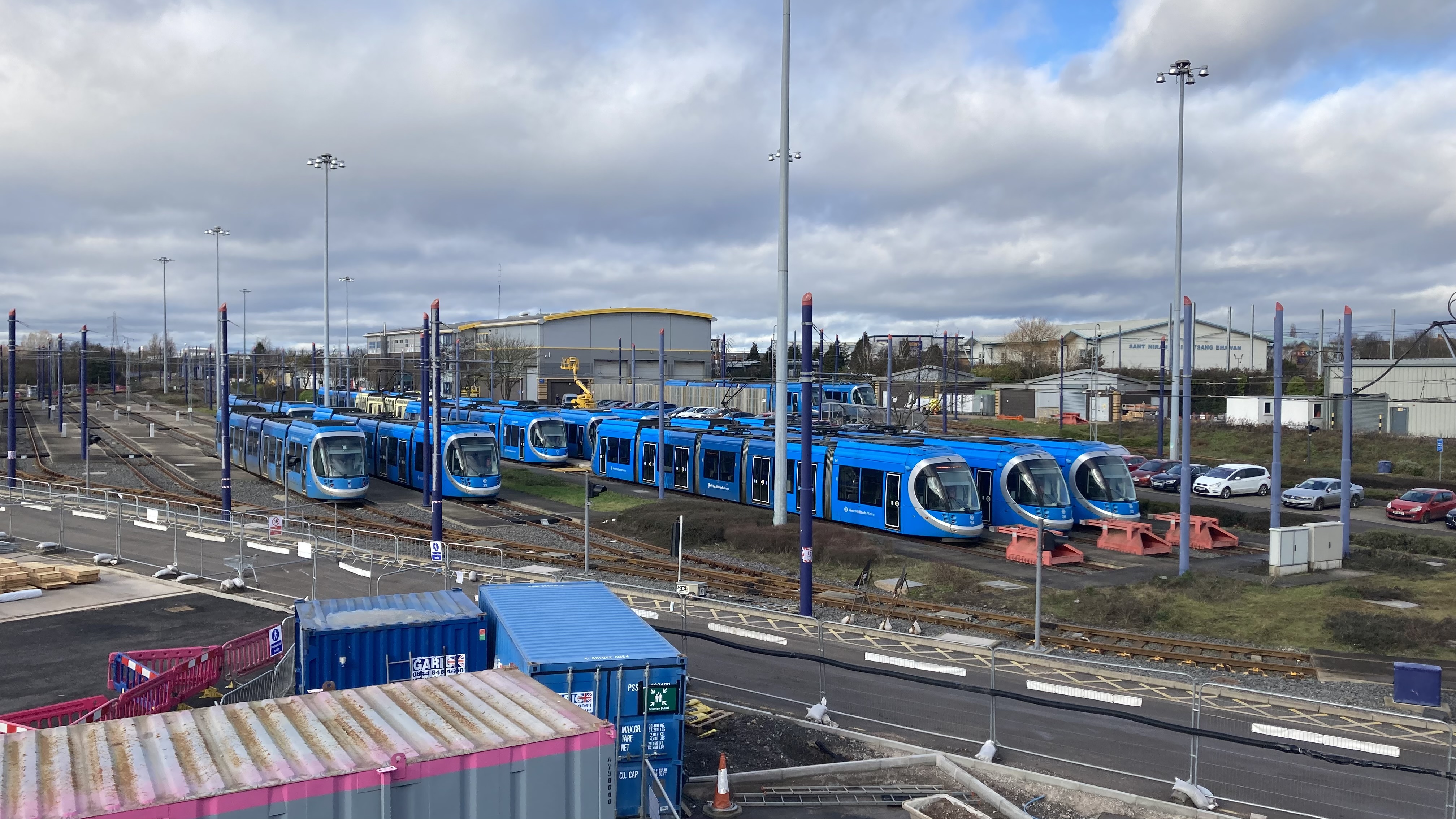 Overlooking depot where more than ten bright blue West Midlands Metro trams are parked up