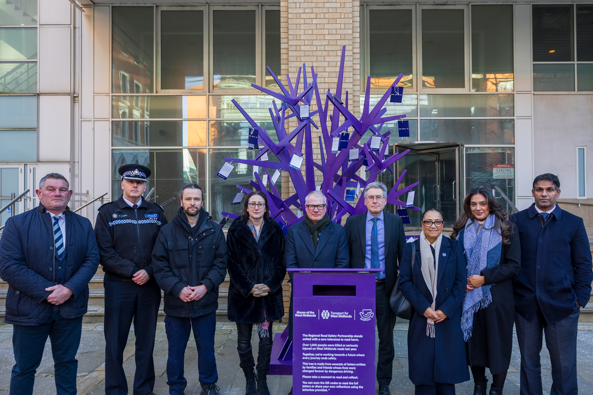 Group of people lined up in front, with the purple  tree towering over them.