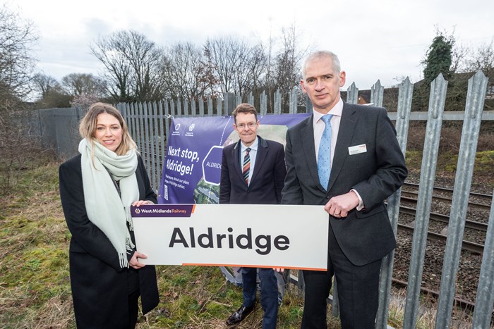 Kate Trevorrow, TfWM rail delivery director, Andy Street Mayor of the West Midlands and Rob McIntosh, managing director for Network Rail's North West and Central Region holding an Aldridge Station sign with the rail line behind a fence in the background