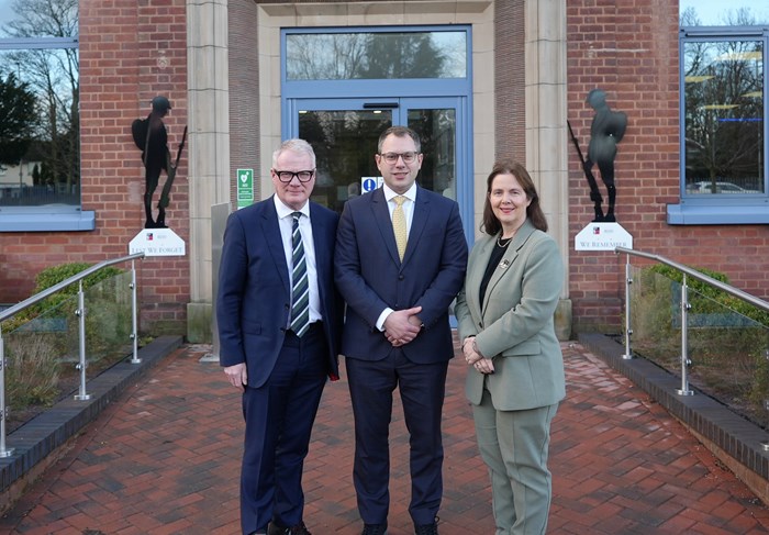 Three individuals in business attire stand outside a brick building with two black silhouette soldier statues.