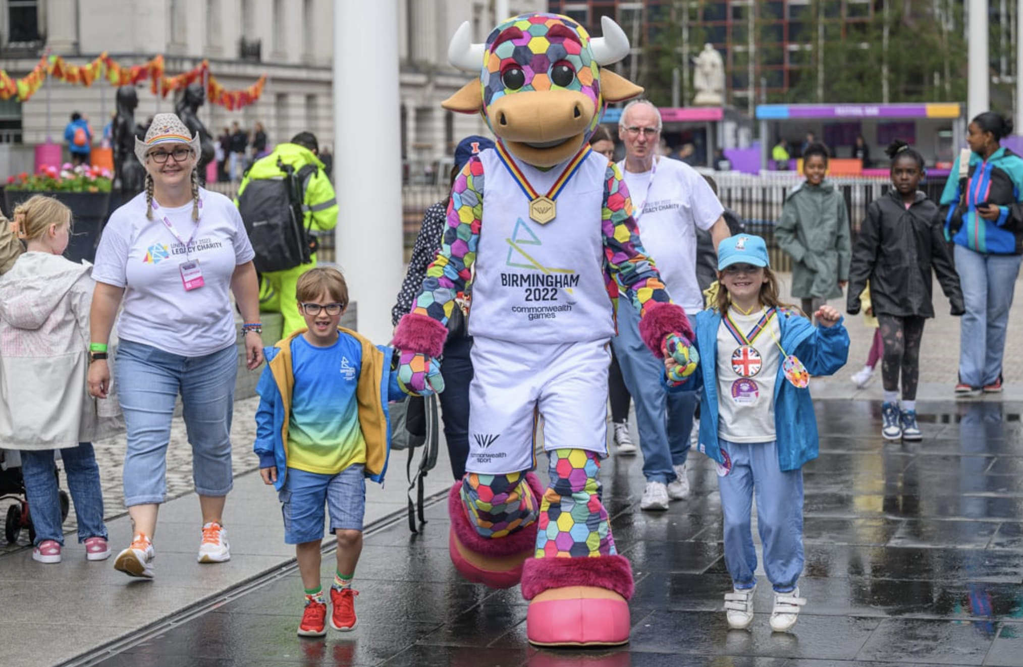 People walking hand in hand wearing Birmingham 2022 merchandise alongside Games' mascot Perry the Bull 