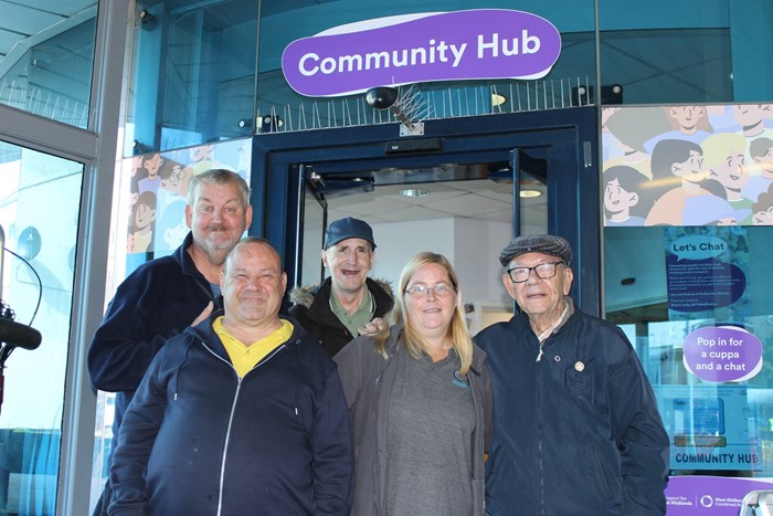 Group of five people, men and women, smiling outside a shop unit with sign above