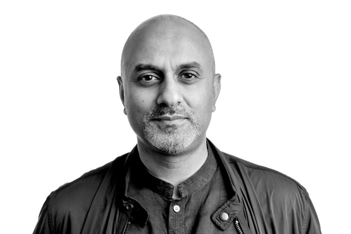 A headshot image in black and white of a man looking directly at the camera. He is wearing a shirt with a jacket on top.