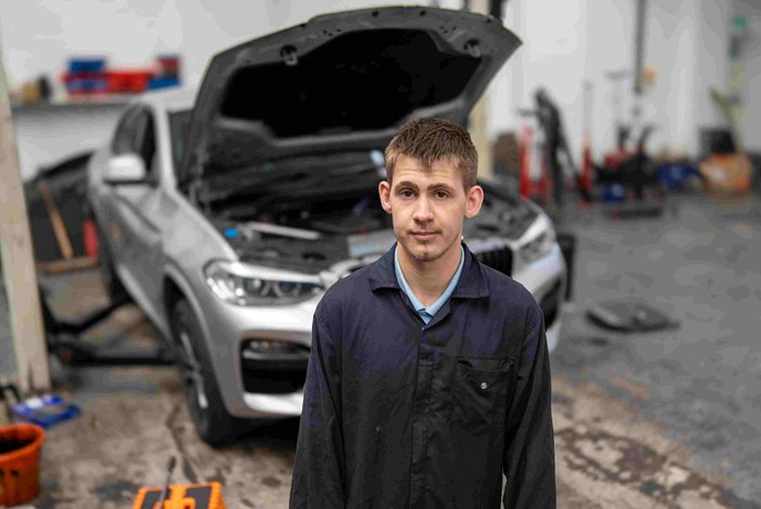 Ben Challice at his place of work - Rehal Autohaus in front of a car with open bonnet