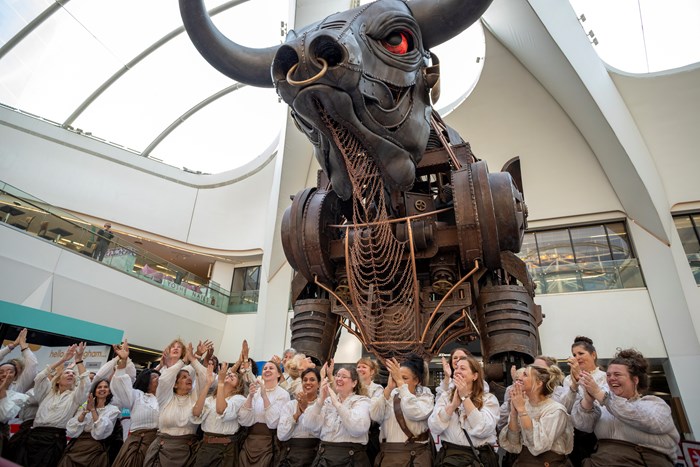 Ozzy the bull sculpture standing in New Street Station concourse with choir dressed as historic women chainmakers