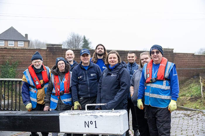 A group of people smiling at the camera on the side of a canal standing in front of a canal lock